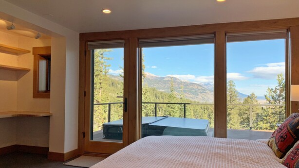 Ein Schlafzimmer mit einem großen Bett, einem Schreibtisch und Bergblick durch raumhohe Fenster.