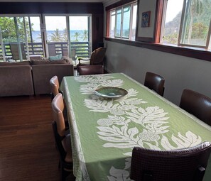 A dining area with a table covered in a green tablecloth with white floral patterns, surrounded by wooden chairs.