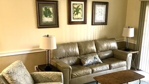 A living room with a leather sofa, a patterned armchair, a small coffee table, and a rug. There are three framed pictures on the wall. - Beautiful  2B/2B, ground floor condo in Riverwalk on Arrowhead Golf course ! (Myrtle Beach)