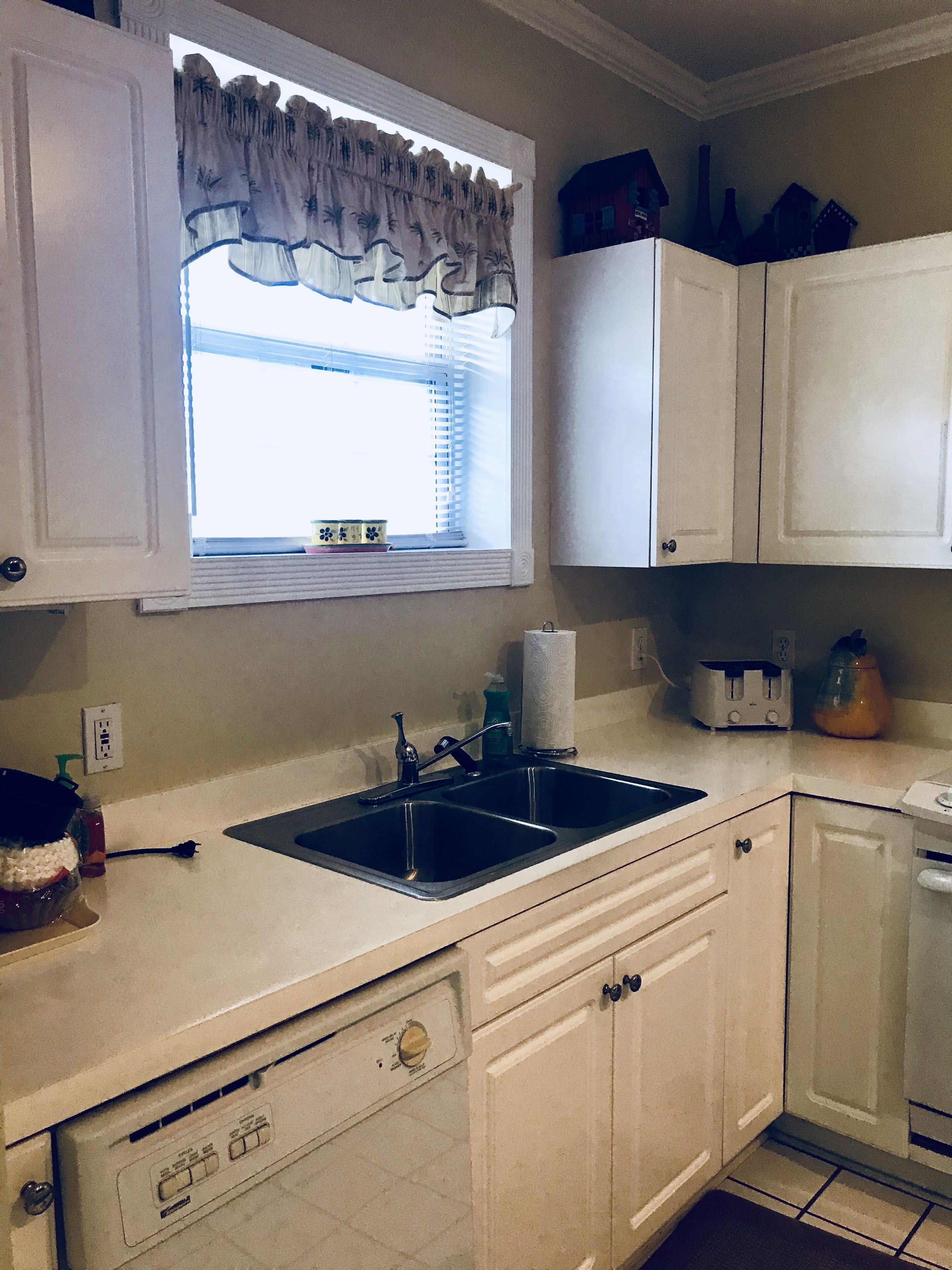 A kitchen with a double sink, a window with a decorative valance, and white cabinetry.