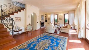 A spacious living area with a blue patterned rug, a staircase with ornate metal railings, and a fireplace.