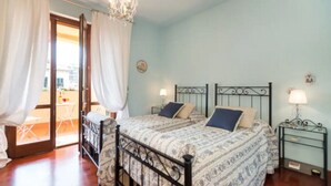 A bedroom with two beds, a chandelier, and a balcony visible through the door.