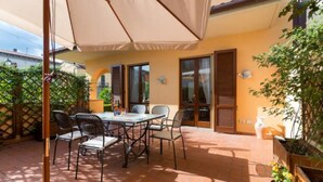 An outdoor patio with a table and chairs, a pergola providing shade, and a view of the street.
