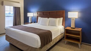Una habitación de hotel con una cama grande, dos mesitas de noche y un ventanal con cortinas.