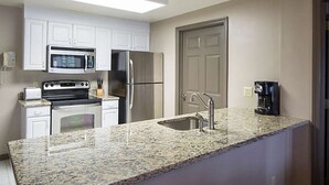 Una cocina con armarios blancos, electrodomésticos de acero inoxidable, encimeras de granito y una cafetera.