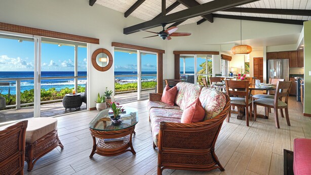 A spacious living area with a large sofa, dining table, and chairs, overlooking a scenic ocean view. - Hale Ohe | Historic Beachfront Home with A/C + Baby Beach (Koloa)