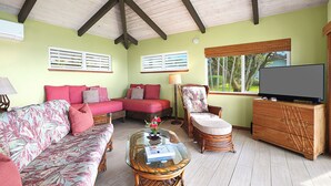 A living room with a sofa, armchair, and a glass coffee table. - Hale Ohe | Historic Beachfront Home with A/C + Baby Beach (Koloa)