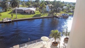 Blick auf einen Kanal mit Booten, einen Pool und eine Terrassenanlage mit Sonnenschirmen und Stühlen.