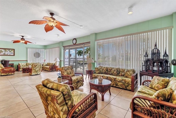A spacious living room with tropical-themed furniture, large windows, and ceiling fans.