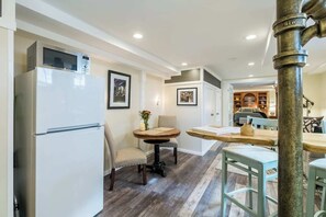A compact kitchen with a refrigerator, a dining table with chairs, and a small round table with a vase.