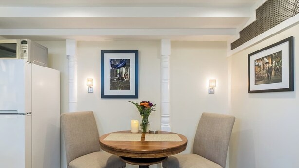 A dining area with a round wooden table, two upholstered chairs, a vase with flowers, and framed pictures on the walls.