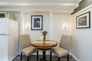 A dining area with a round wooden table, two upholstered chairs, a vase with flowers, and framed pictures on the walls.