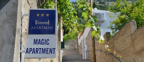 A sign for 'Magic Apartment' with a five-star rating, located at the top of a staircase in a residential area with stone walls and greenery.