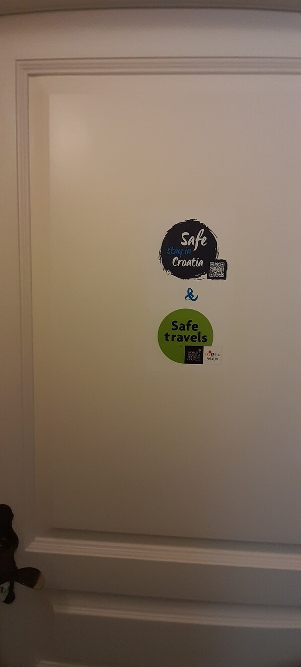 A white door with two stickers, one black and one green, with text and a QR code. - THE MAGIC APARTMENT - A most pleasant stay with an amazing view! (Dubrovnik)