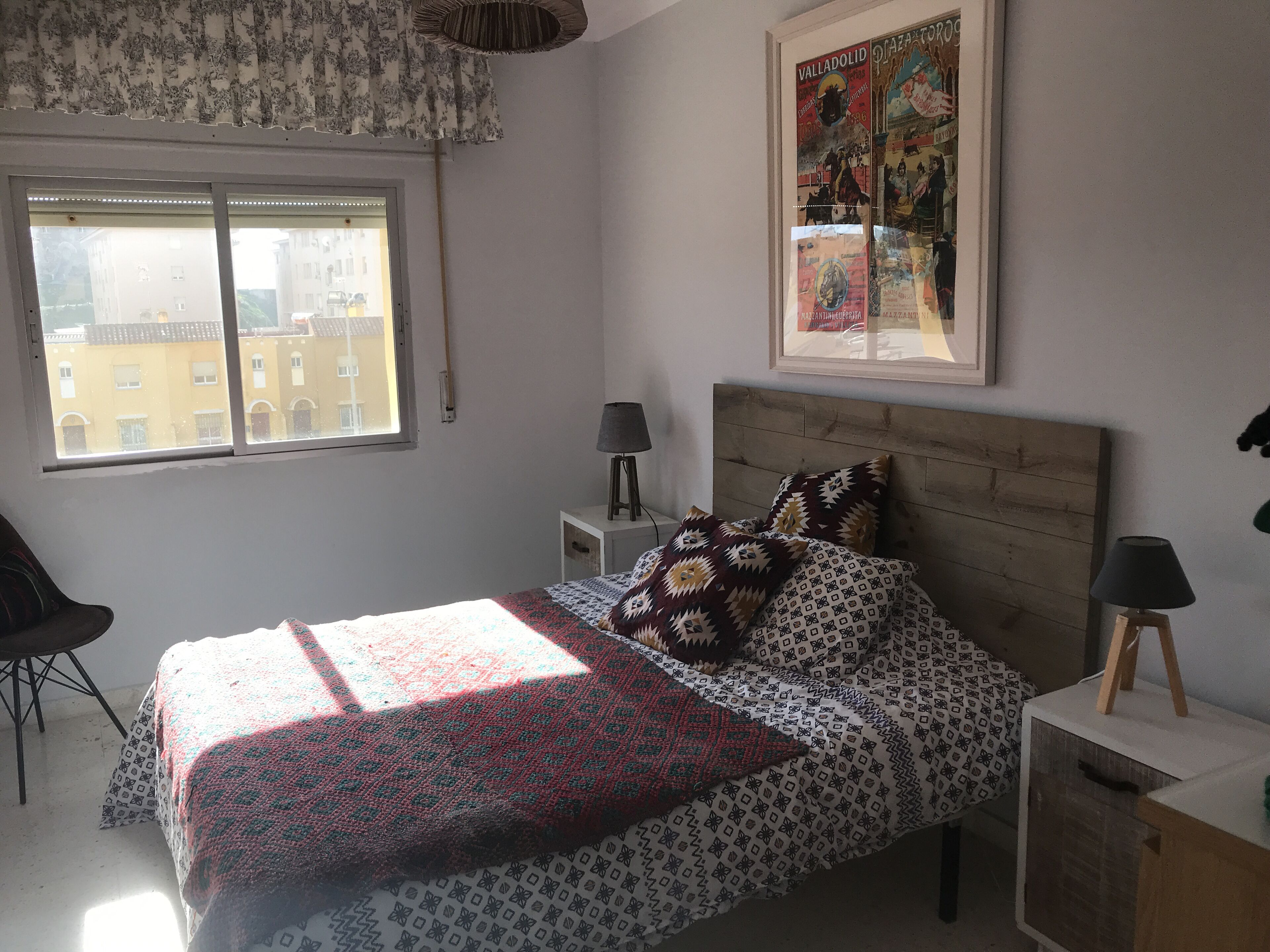 Une chambre à coucher comprenant un lit, deux tables de chevet, une chaise, une fenêtre et un tableau accroché au mur.