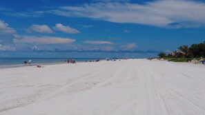 Ein weiter Sandstrand mit blauem Himmel und vereinzelten Personen am Ufer.