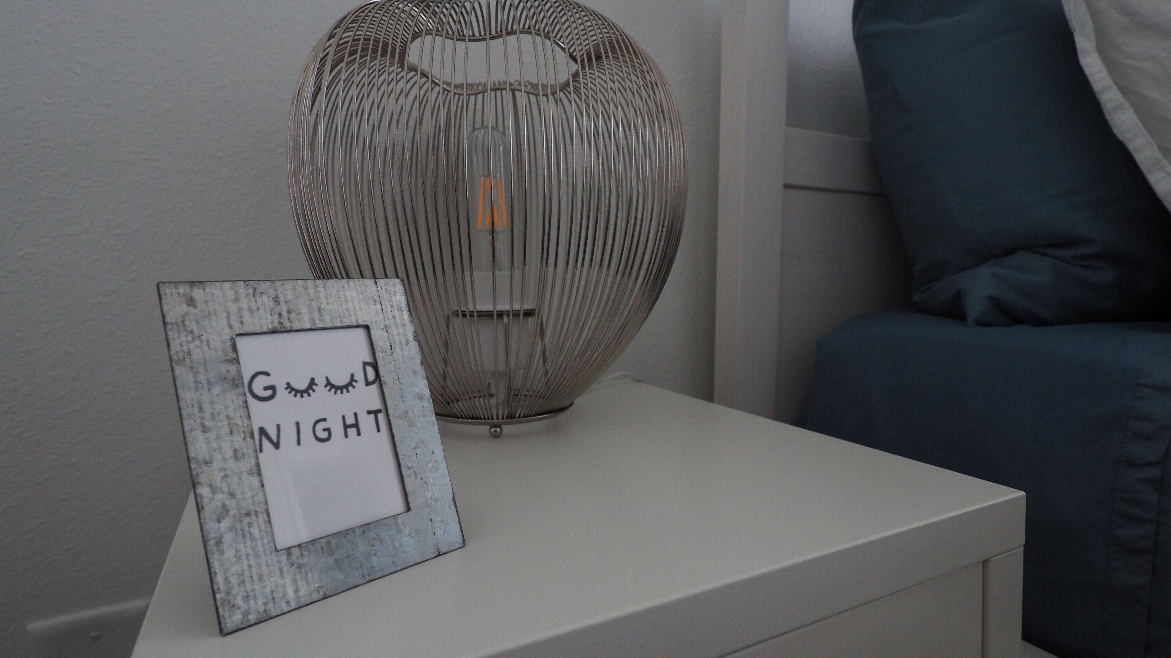 Ein Nachttisch mit einer dekorativen Metalllampe und einem gerahmten Schild mit der Aufschrift 'Good Night'.