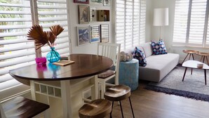 A modern living room with a round wooden dining table, white chairs, a blue accent chair, a grey sofa with patterned cushions, and a small round table with a lamp. - Relax near St. Pete & Clearwater Beaches, stay in our 2-bedroom beach condo (Indian Rocks Beach)