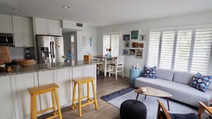 A modern kitchen with white cabinets, a granite countertop, and stainless steel appliances. There is a dining area with a white table and chairs, and a living room with a grey sofa and a coffee table. - Relax near St. Pete & Clearwater Beaches, stay in our 2-bedroom beach condo (Indian Rocks Beach)