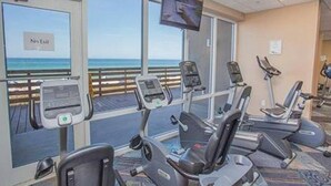 A fitness room with treadmills and exercise equipment, large windows with a view of the beach, and a television mounted on the wall. - Royal Beachfront Unit, Sleeps 6, Walk to Pier Park (Panama City Beach)