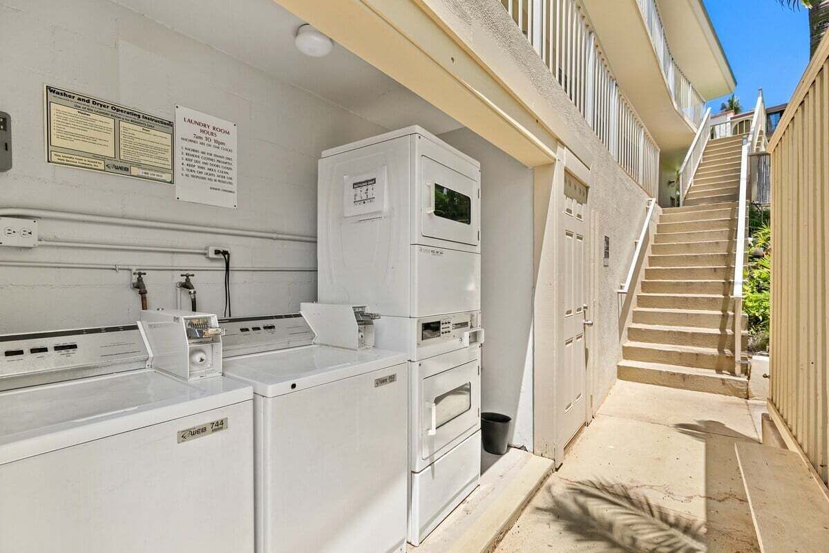 A laundry room with stacked washers and dryers, a sign with operating instructions, and a staircase leading to an upper level.