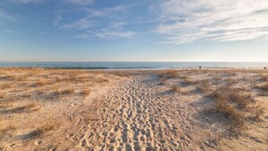 En sandstrand med fodaftryk, der fører ned mod vandet, en klar himmel og en fjern horisont.