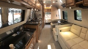 A compact RV interior with a kitchenette, a sofa, and a dining area. - RIVERFRONT Lush&Lux AIRSTREAM Cabin Stunning Views (Three Rivers)