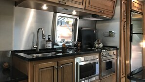 A compact kitchen with wooden cabinets, a stainless steel sink, a built-in oven, and a refrigerator. - RIVERFRONT Lush&Lux AIRSTREAM Cabin Stunning Views (Three Rivers)