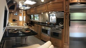 A compact RV kitchen with wooden cabinets, a stainless steel refrigerator, a microwave, and a stove. - RIVERFRONT Lush&Lux AIRSTREAM Cabin Stunning Views (Three Rivers)