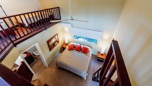 A bedroom with a bed, a window, a ceiling fan, and a staircase.