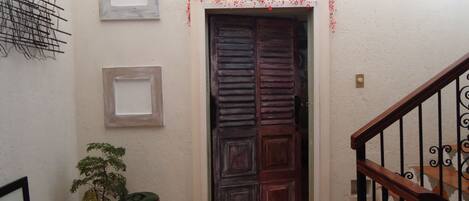 Un pasillo con una puerta de madera, una pequeña planta en maceta y un cuadro en la pared.