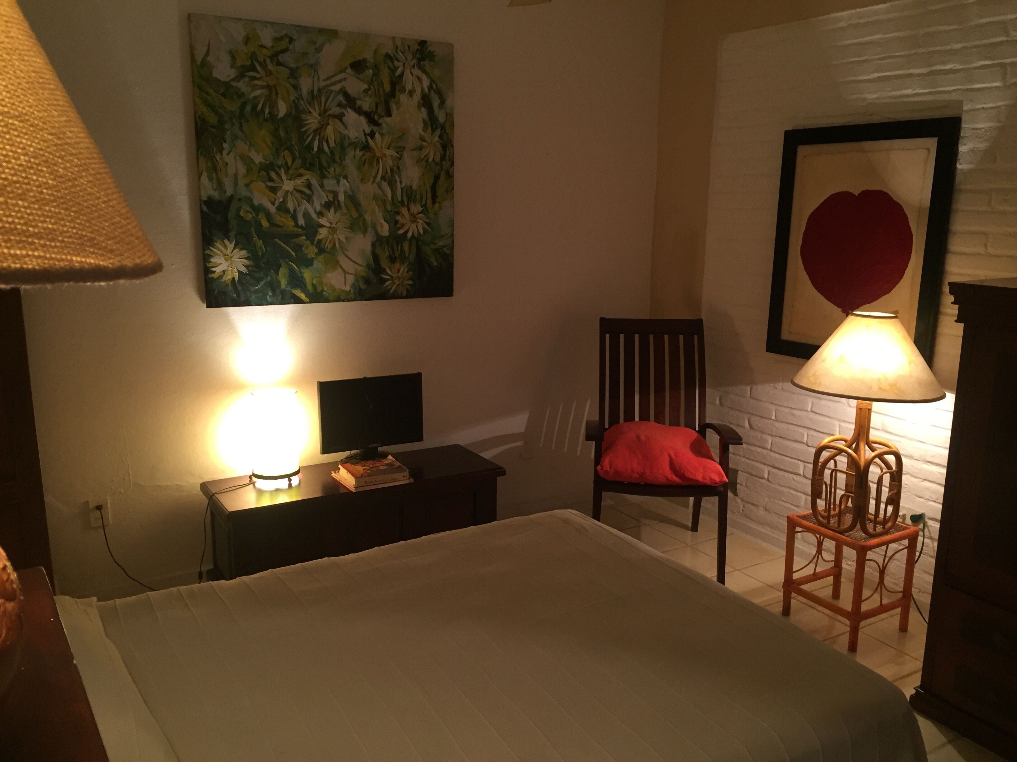 Een kamer met een bed, een bureau met een lamp, een stoel, een muurschildering en een ingelijst kunstwerk.