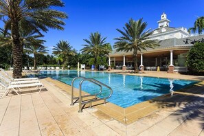 Una piscina con sillas de descanso, palmeras y un edificio con torre.