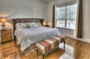 Un dormitorio con cama, mesitas de noche, un banco y una ventana con cortinas.