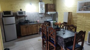 Una cocina con refrigerador, microondas, estufa y mesa de comedor con sillas.