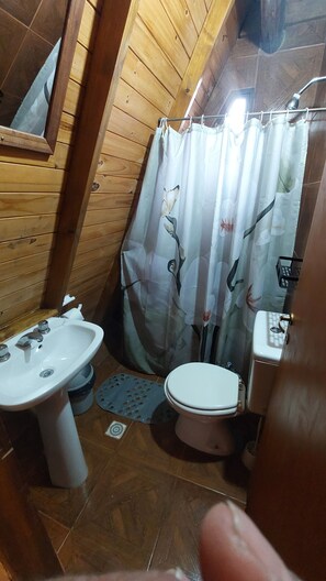 Un baño con detalles de madera, un lavamanos blanco, un inodoro y una cortina de ducha con estampado floral.