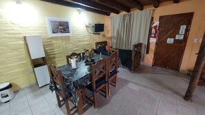 Un comedor con una mesa dispuesta para cuatro personas, rodeada de sillas de madera. Un televisor está montado en la pared sobre la mesa.