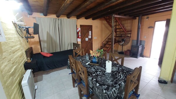 Une pièce comprenant un lit, une table avec des chaises, un ventilateur et un escalier.