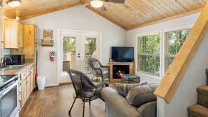 Un intérieur chaleureux comprenant une cuisine, un coin repas et un salon, avec des plafonds en bois, une cheminée et de grandes fenêtres.