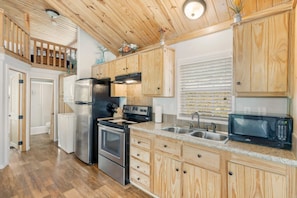 A kitchen with wooden cabinets, a stainless steel refrigerator, an oven, a microwave, and a sink.