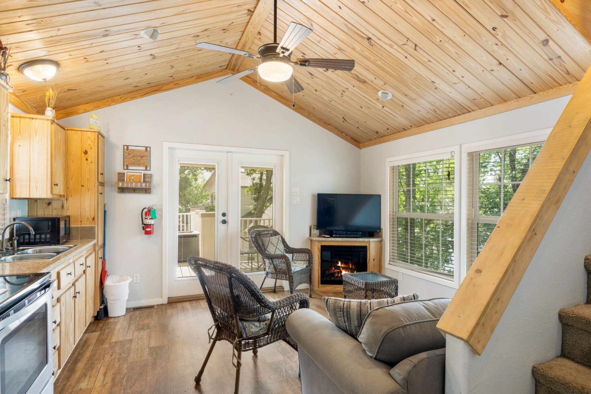 A cozy interior with a kitchen, dining area, and living room, featuring wooden ceilings, a fireplace, and large windows.