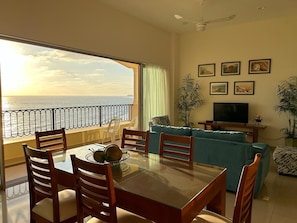 A living room with a balcony overlooking the sea, a dining table with chairs, a sofa, and a TV on a stand. - BEAUTIFUL, LUXURY Mazatlan Condo Right on Beach!! (Mazatlán)