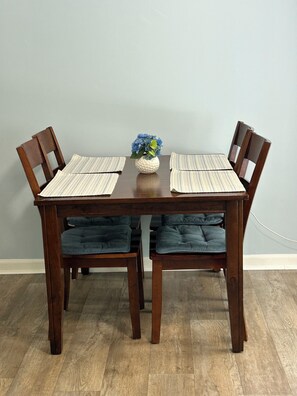 A dining table with four chairs, a vase with flowers, and striped placemats.