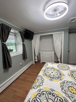A bedroom with a bed, a dresser, a ceiling fan, and a window with curtains.