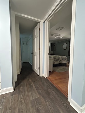 A hallway leading to a bedroom with a bed, a dresser, and a mirror on the wall.