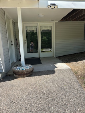 A house with a covered porch, a wooden barrel with pebbles, and a door with a glass panel.