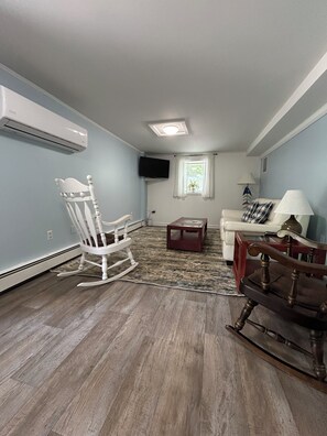 A living room with a white rocking chair, a sofa, a coffee table, and a television mounted on the wall.