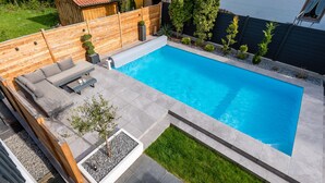 Una piscina rectangular con cubierta de madera y un área de estar integrada.