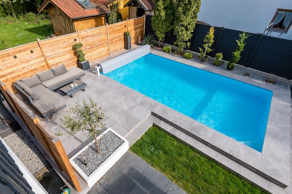 Una piscina rectangular con cubierta de madera y un área de estar integrada.