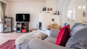 Una sala de estar con un sofá gris, cojines rojos, un televisor, una estantería y un adornado en la pared.